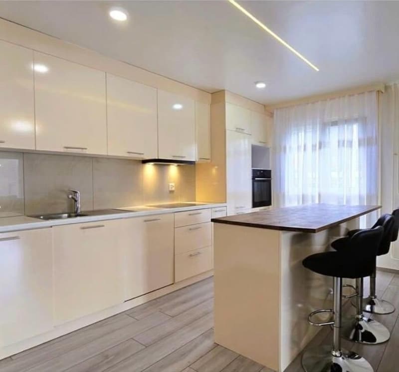 modern kitchen with white cabinets, wooden countertop, stainless steel sink, faucet, black bar stools, white appliances