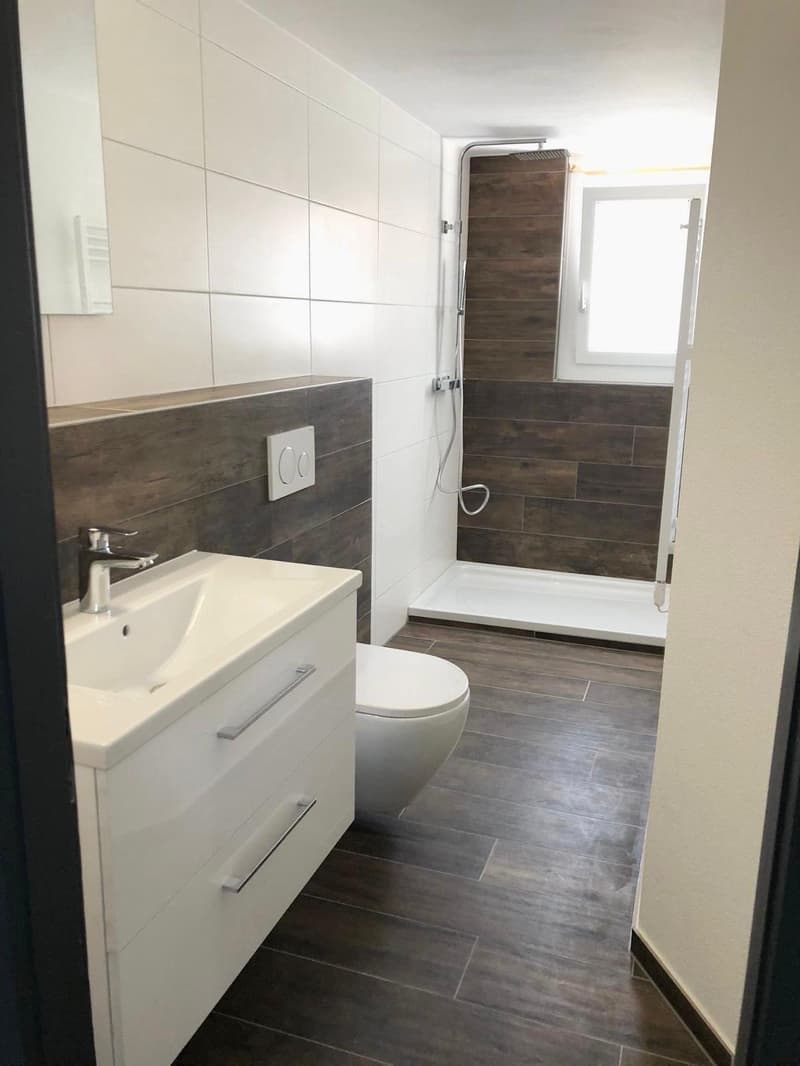Bathroom with white tiles, wooden floor, white sink, white toilet, shower area with wooden wall