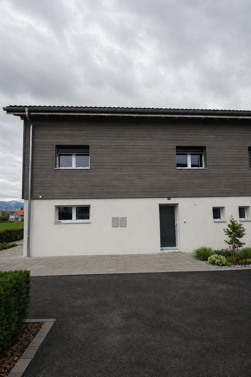 modern house, gray and white exterior, large windows, entrance with glass door, paved driveway, small garden