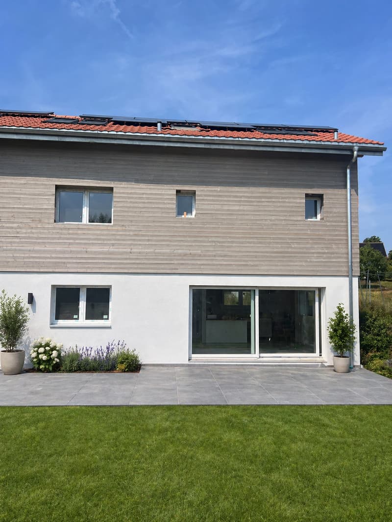 2 story house, wooden and white exterior, solar panels on roof, large glass doors, garden with plants