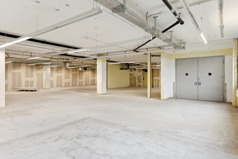 Empty room with concrete floor, unfinished walls, metal beams, and fluorescent lights