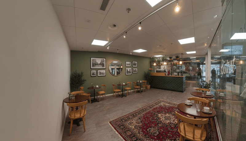 A coffee shop with wooden tables and chairs, green walls, a mirror, and a counter with a brick wall.