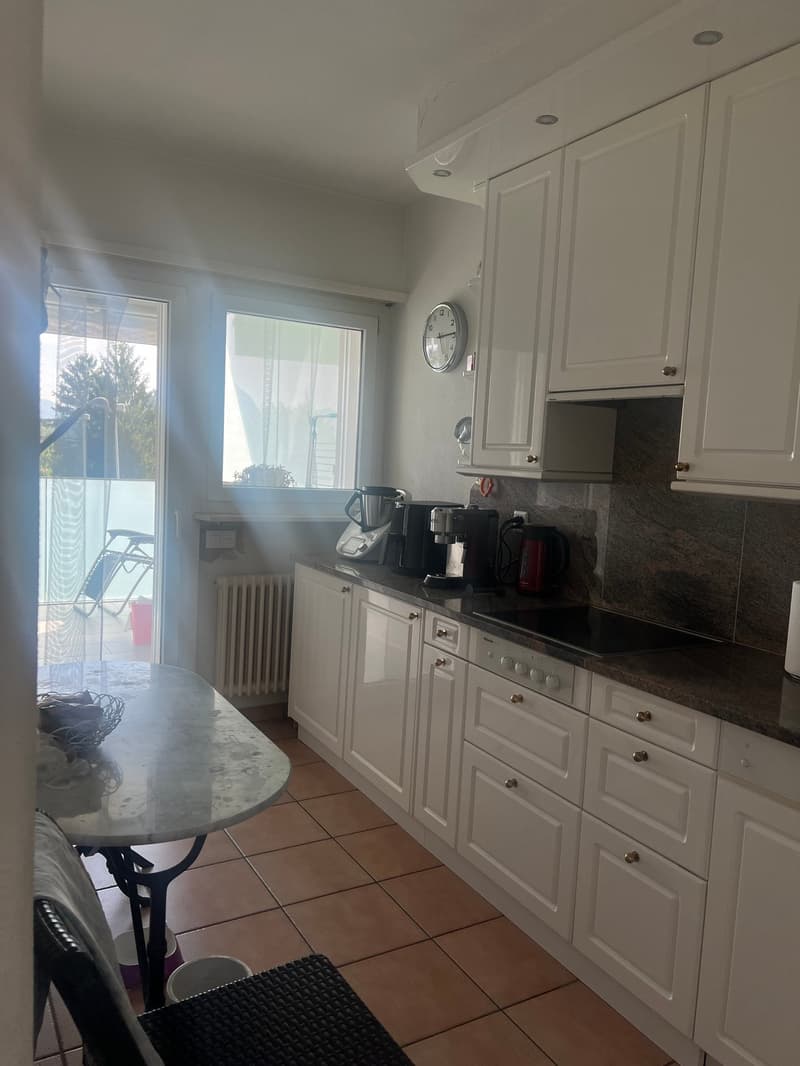 White cabinets, black countertops, tile flooring, kitchen appliances including a dishwasher, and a small dining table