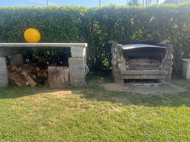 Outdoor stone fireplace, wood storage area, grassy area, hedges in the background