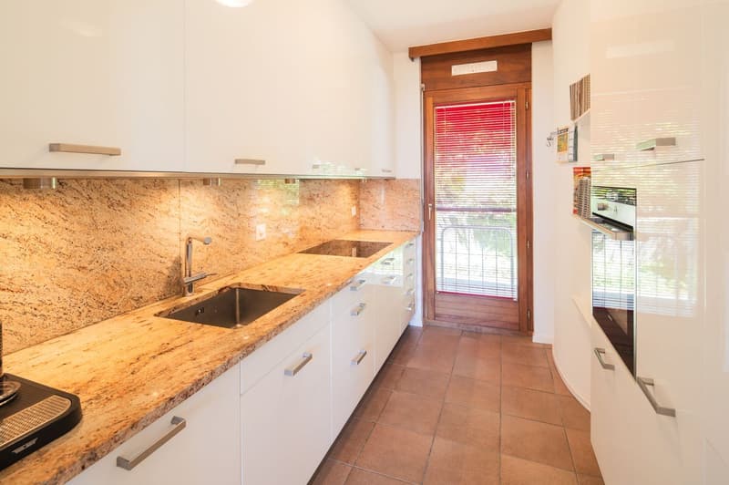 Spacious kitchen with granite countertops, white cabinets, stainless steel sink, and a dishwasher. The kitchen has a sliding glass door leading to the exterior. The floor is tiled and the walls have a neutral color scheme.