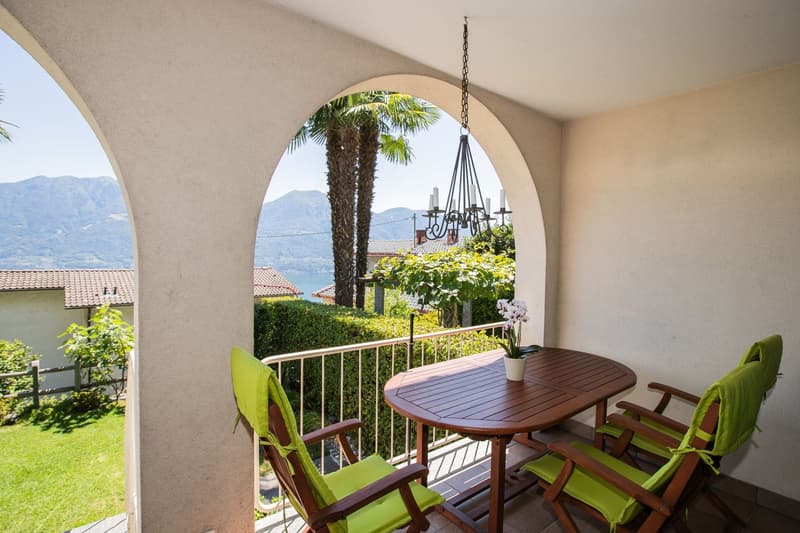Covered balcony with a round arch, wooden table and chairs, overlooking a scenic view of palm trees and mountains