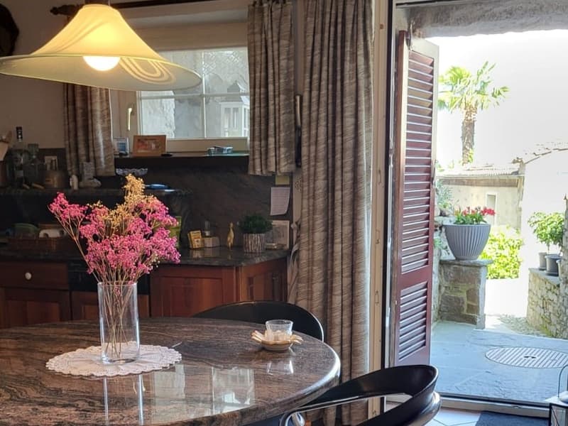 Cozy living room with a round wooden table, a vase of pink flowers, and a view of the outdoor patio through the large glass doors.