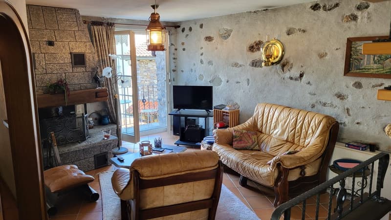Rustic living room with stone walls, leather sofa and armchair, fireplace, TV, and decorative accents