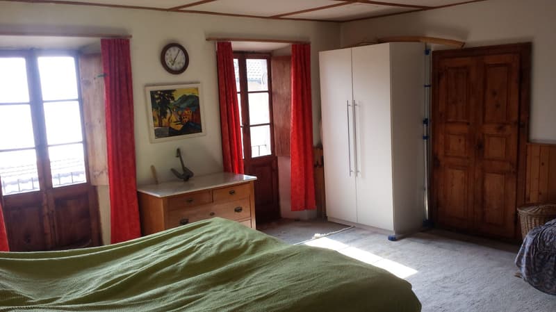 Bedroom with wooden doors and window, large bed, wooden cupboard, painting, clock, white floor