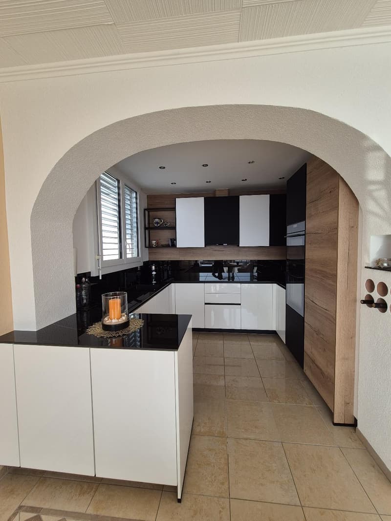 modern kitchen with white cabinets, black countertops, wooden flooring, and an arched ceiling