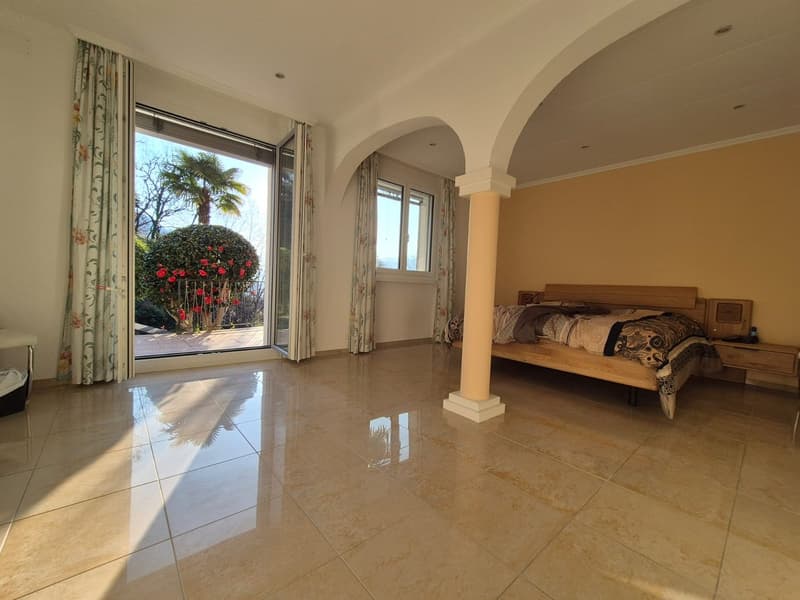 large bedroom, double bed, wooden headboard, nightstand, large windows, sliding glass door, balcony, tiled floor, curtains