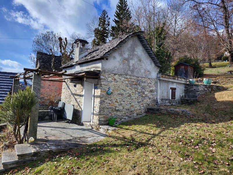 Single-story stone cottage, chimney, exterior porch, outdoor seating, small garden