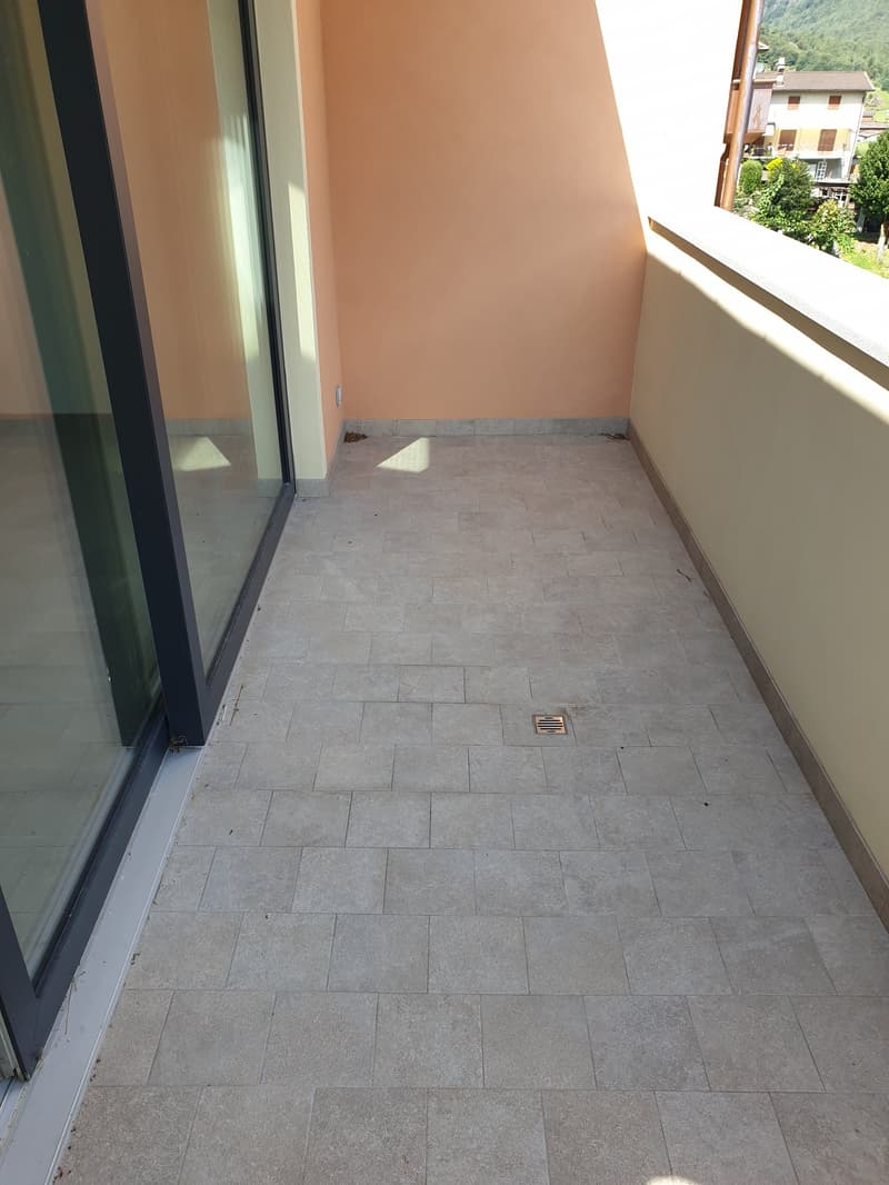 Empty balcony, tiled floor, glass railing, no visible furniture