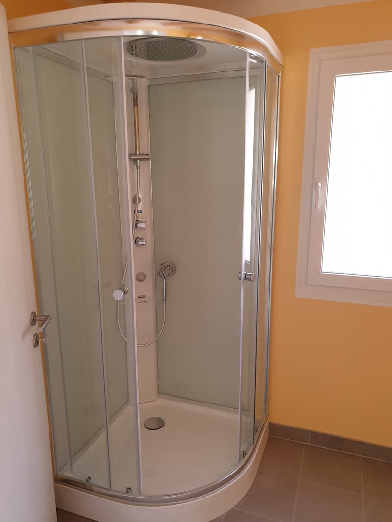 Enclosed glass shower with shower head, shower hose, and a window to let in natural light.