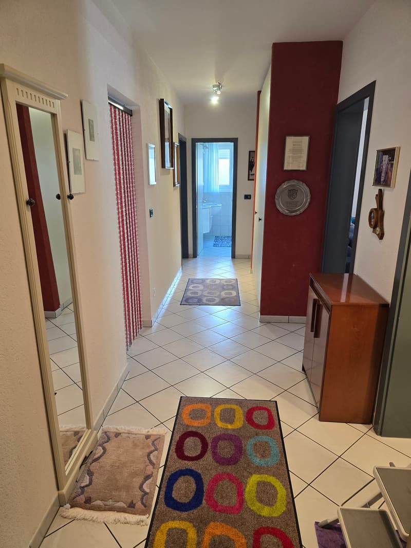 white tiled floor, red and white wall, mirror, wooden cabinet, framed pictures, rug, hallway leading to rooms