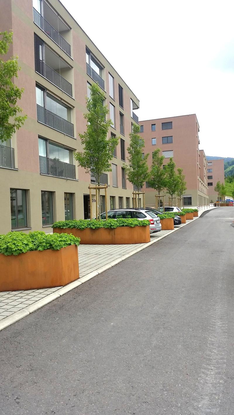Multi-story apartment building with balconies, parking spaces, and landscaping in the front