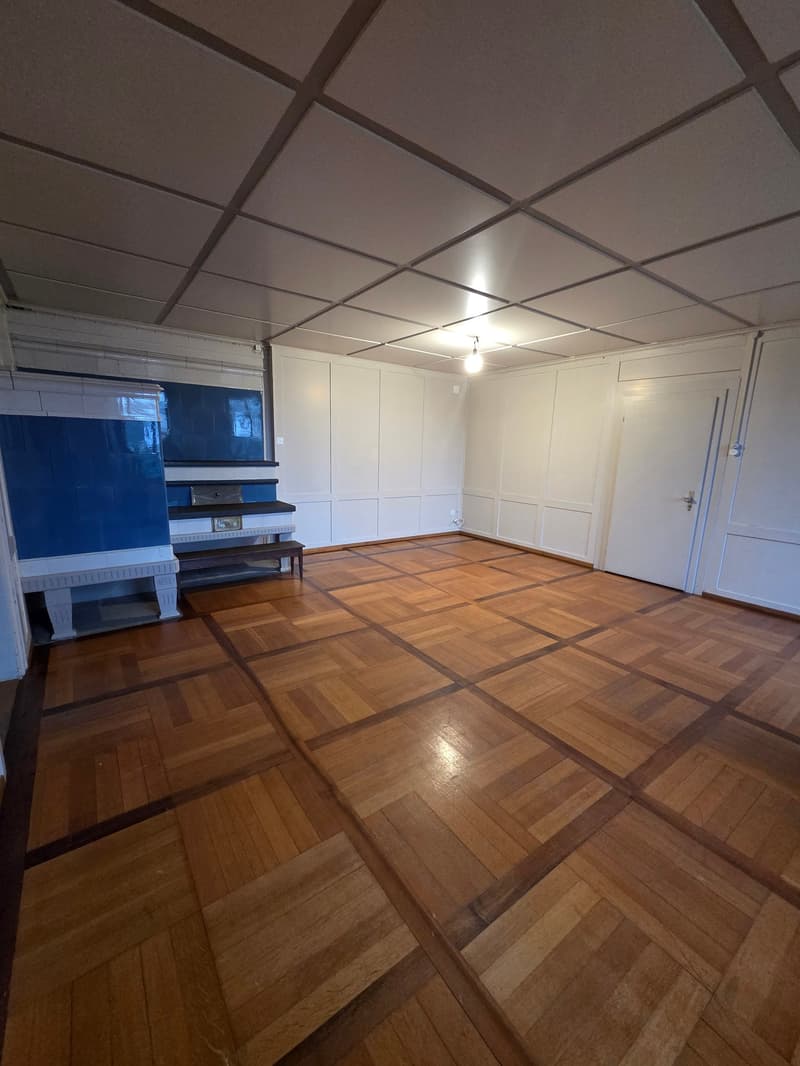 Empty room with wooden floors, white walls, ceiling with square pattern and a bench by a blue wall.