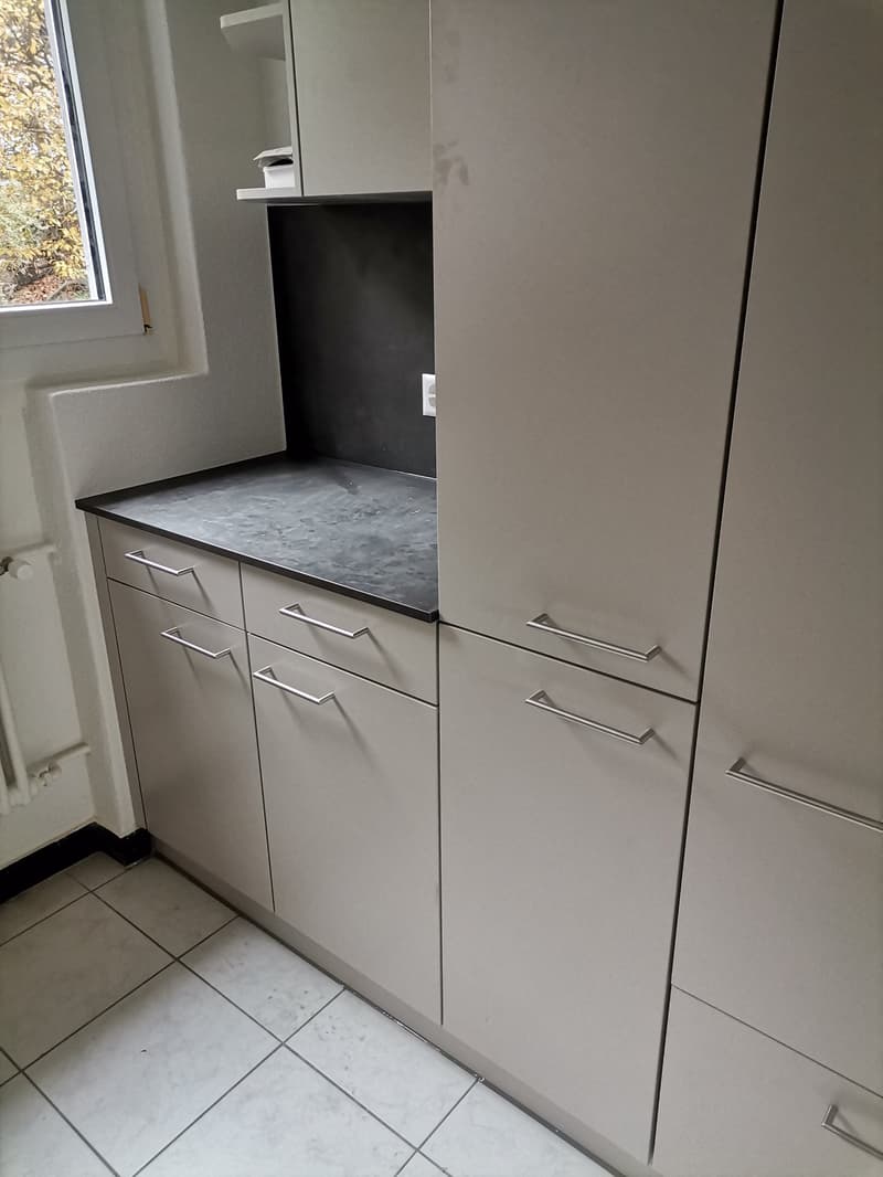 modern kitchen with gray cabinets, black countertop, white tiled floor, window, electrical outlet, and a shelf