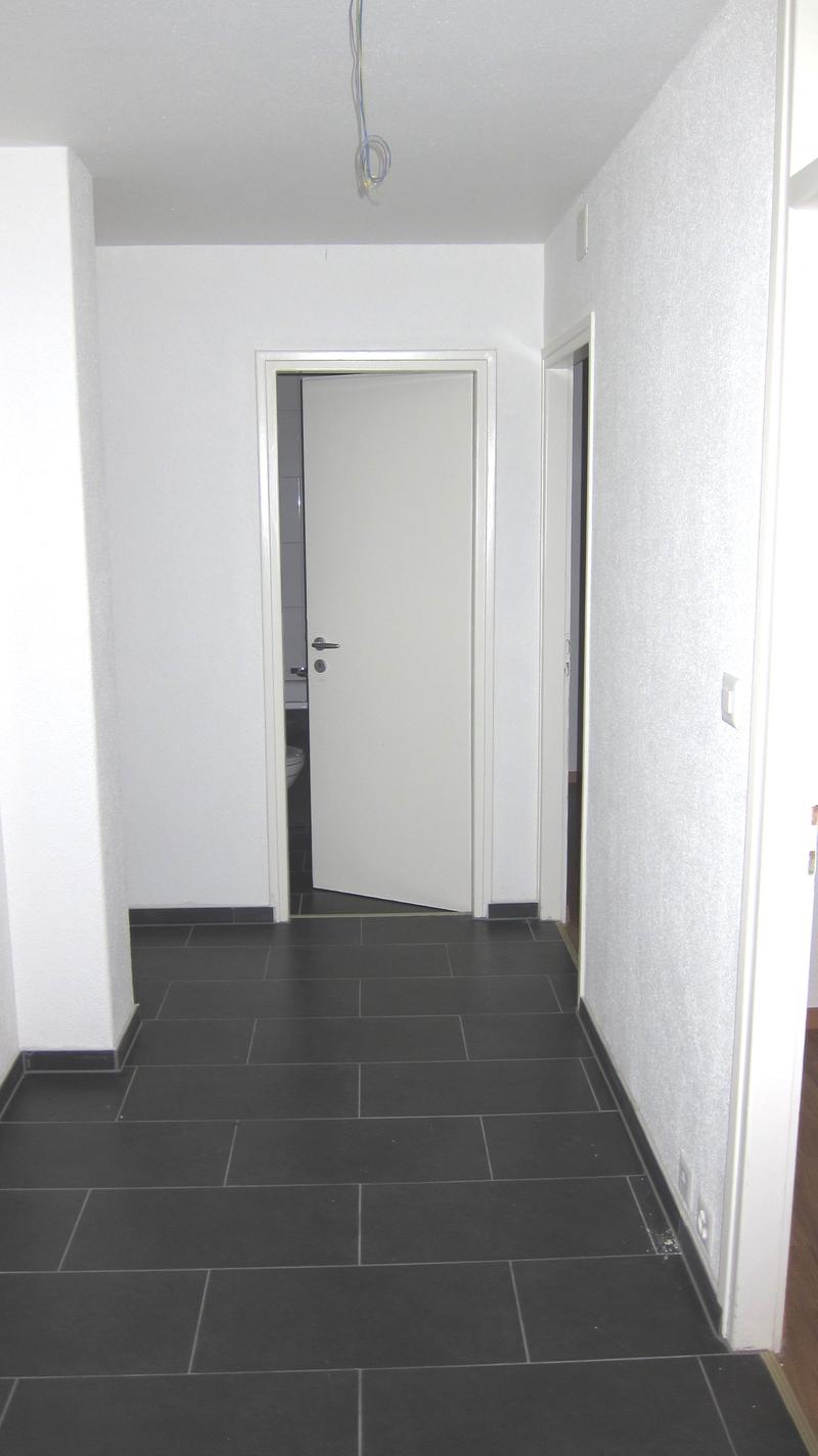 Empty room with white walls, black tiles, white door, and a toilet