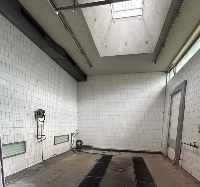 Empty room with white tiled walls, concrete floor, vent in the ceiling, windows, hose, metal grates, drain