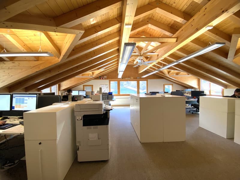Open office space with wooden beams, multiple desks, computers, and a printer.