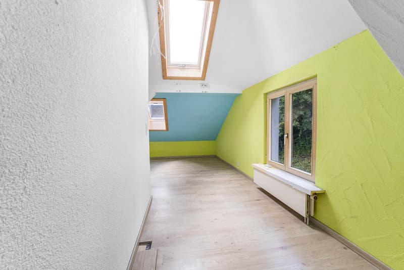 Attic room with slanted ceiling, white walls, green and blue accent walls, hardwood flooring, and a window overlooking the outdoors
