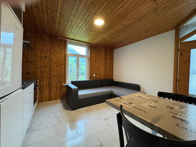 Living room: wooden walls, tiled floor, built-in couch, window, refrigerator, kitchen area, wooden dining table and chairs