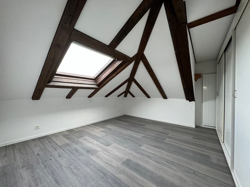 empty attic room with wooden beams, skylight, wooden floor, white walls