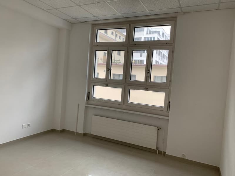 Empty room with white walls and floor, a radiator, large window, and two electrical outlets