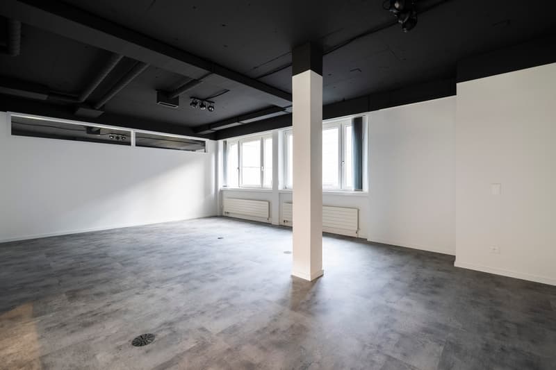 Empty room, concrete floor, white walls, three windows, ceiling lights, a column