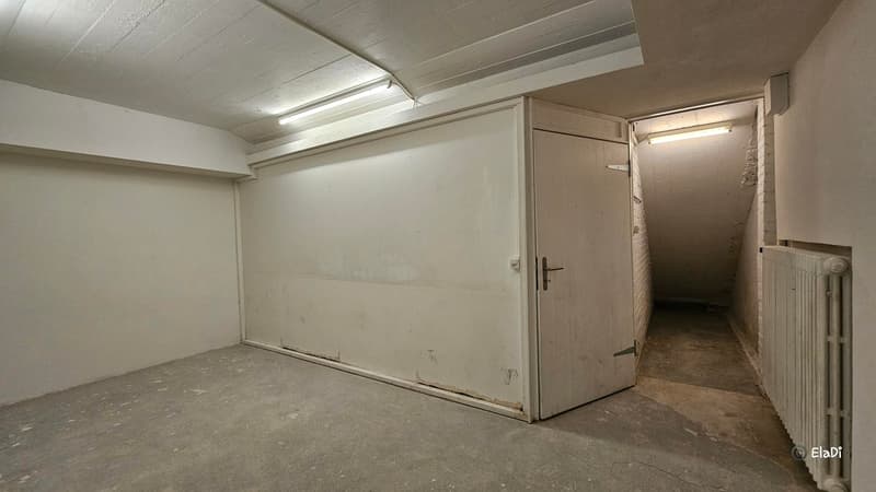 a garage with a white door, ceiling with lights, white wall, floor with concrete