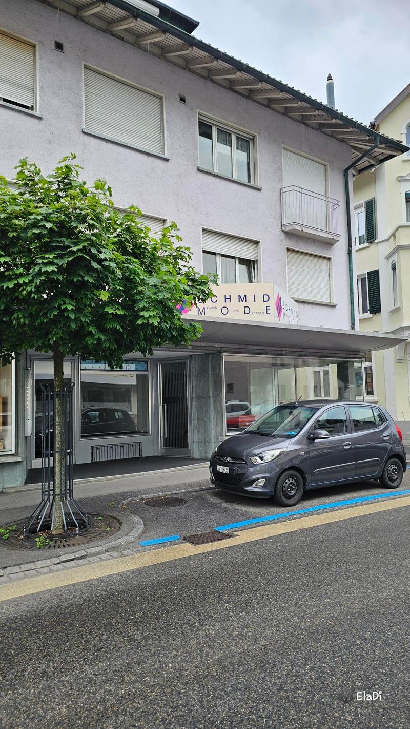 3 story building with balcony, windows, commercial sign on ground floor, black car parked on road
