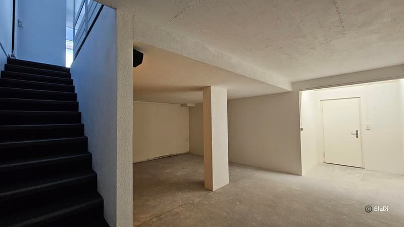 empty room with cement floor, large white pillar, staircase on the left, door on the right