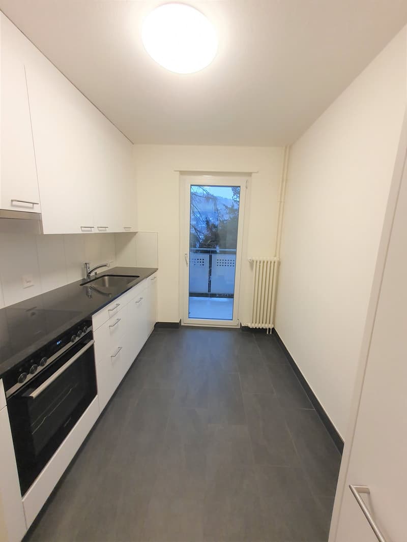 modern kitchen with white cabinets, black countertops, stainless steel sink, oven, and a sliding door leading to a balcony