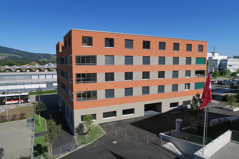 modern office building, orange and gray facade, multiple windows, parking lot, flag