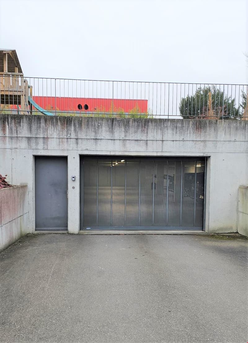 A concrete building with a metal railing on top, two garages, and a slide on the left side.