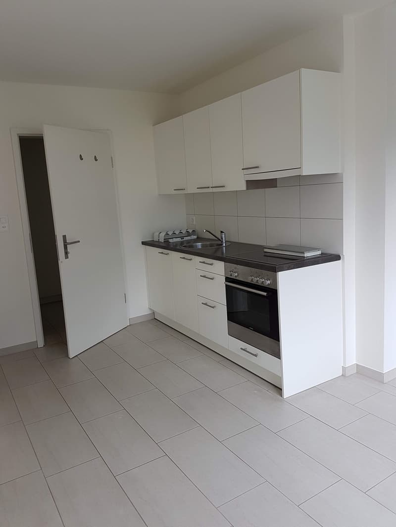 Modern, minimalist kitchen with white cabinets, black countertop, built-in oven and stovetop, and gray tile flooring.