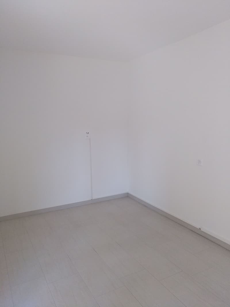 Empty room with white walls and gray tile flooring. The room appears to be a minimalist and unfinished space.
