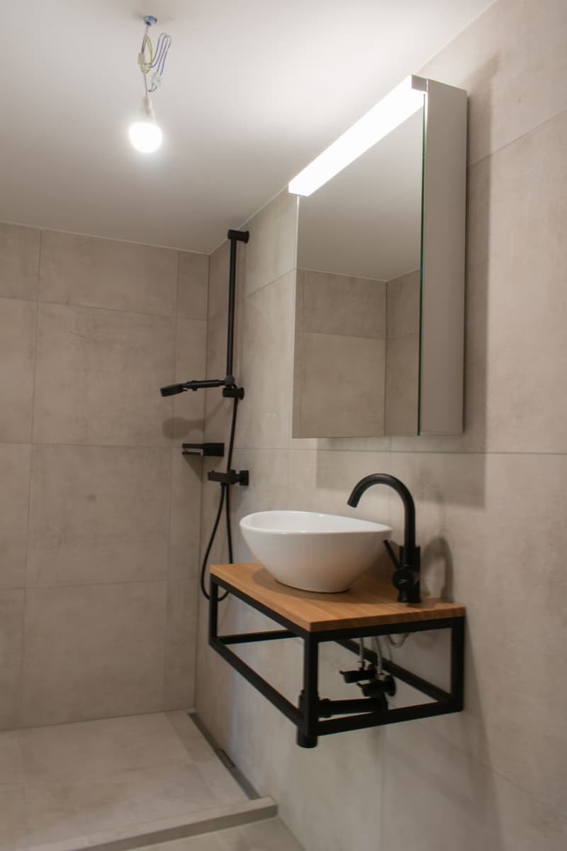 modern bathroom with white sink, black faucet, mirror, shower area, tiled walls