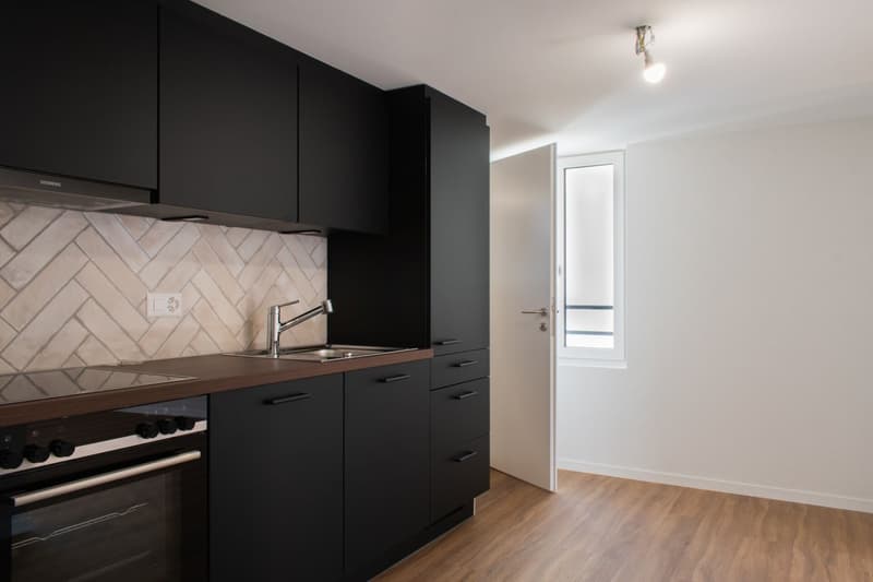 modern kitchen with black cabinets, wooden countertop, stainless steel sink, faucet, oven, extractor hood, white tiles, white walls, wooden floor