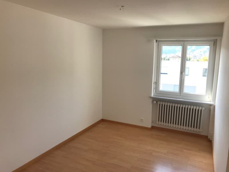 Spacious bedroom with white walls, hardwood flooring, and large windows providing natural light. The room appears to be empty, ready for furnishing and personalization.