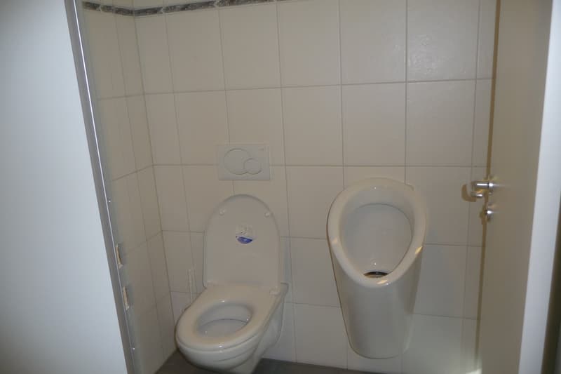 Small bathroom with white toilet and urinal. White walls with tile finish.