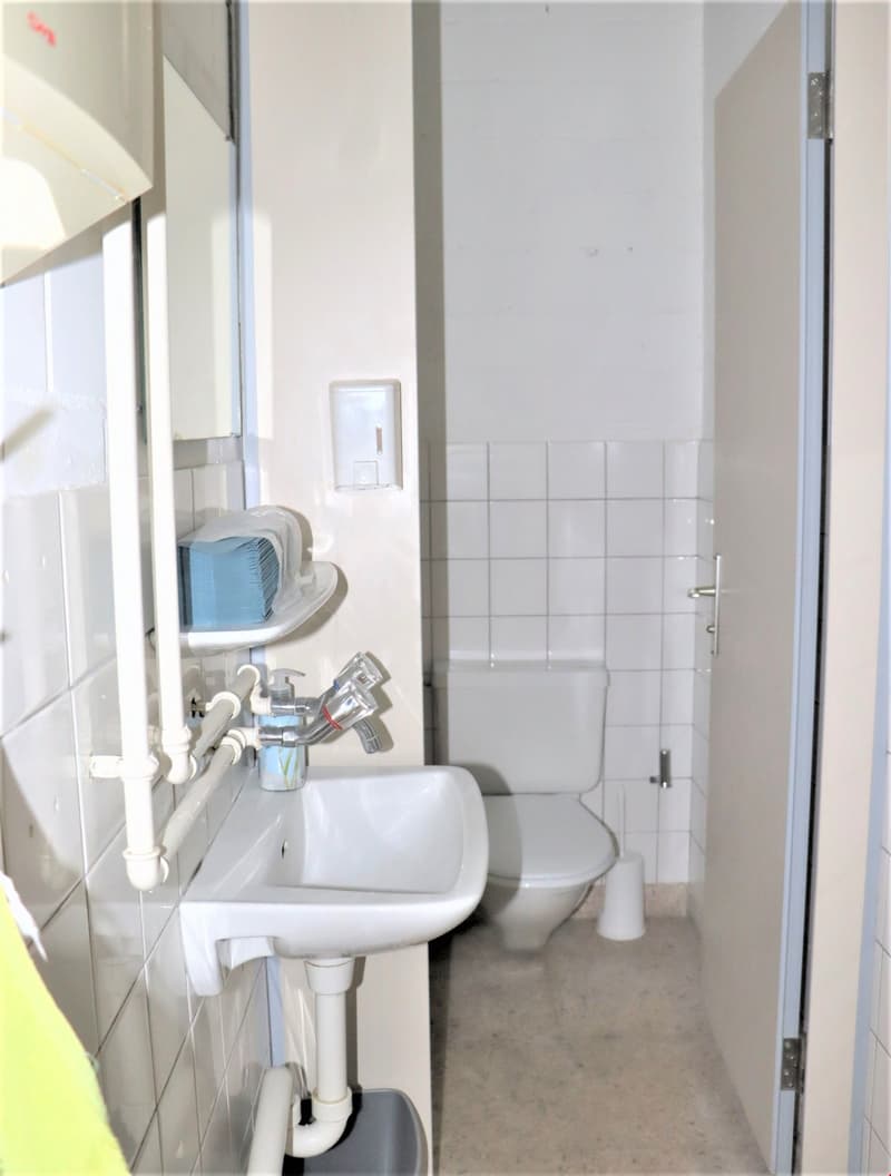 Small bathroom with white tiles, a sink, and a toilet. There is a washing machine visible in the corner.