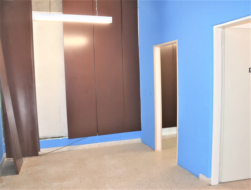 The image shows an interior room with blue walls, a brown cabinet or closet, and a concrete floor. There is a doorway visible in the background.