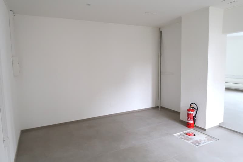 Empty room with white walls, concrete floor, and a fire extinguisher in the corner.