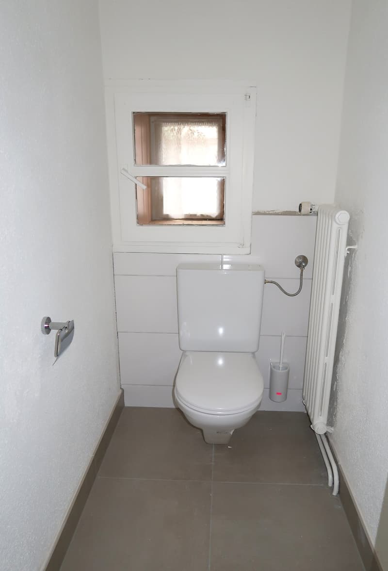 small bathroom with white walls, gray floor, toilet, and a radiator