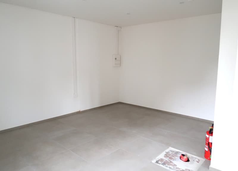 Empty room with white walls and gray tile flooring. There is an electrical panel on the wall.