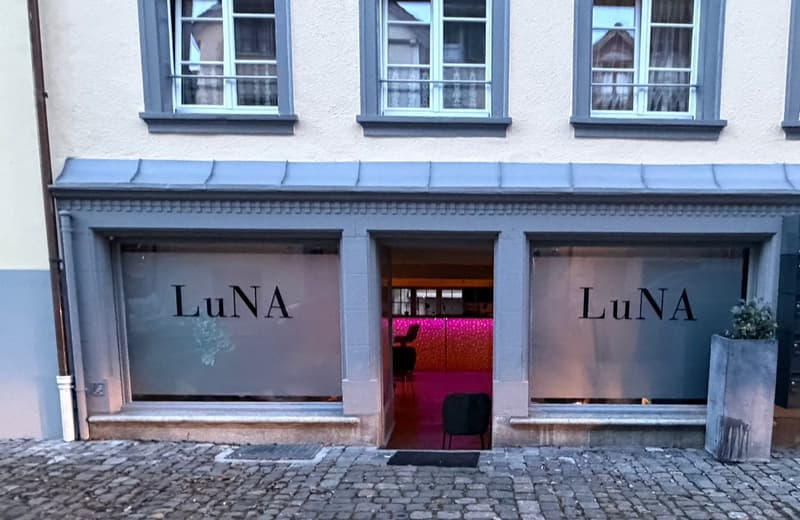 Facade of building with 3 glass windows on the top floor and 2 glass display windows, entrance with a pink interior