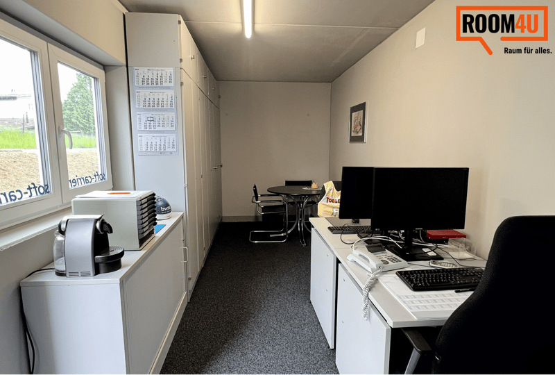 Office with desk, computer, chair, table, calendar, coffee machine, and storage cabinets.