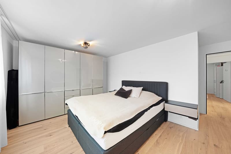modern bedroom with a large bed, white walls, wooden floor, built-in wardrobes, bedside table, and a ceiling light